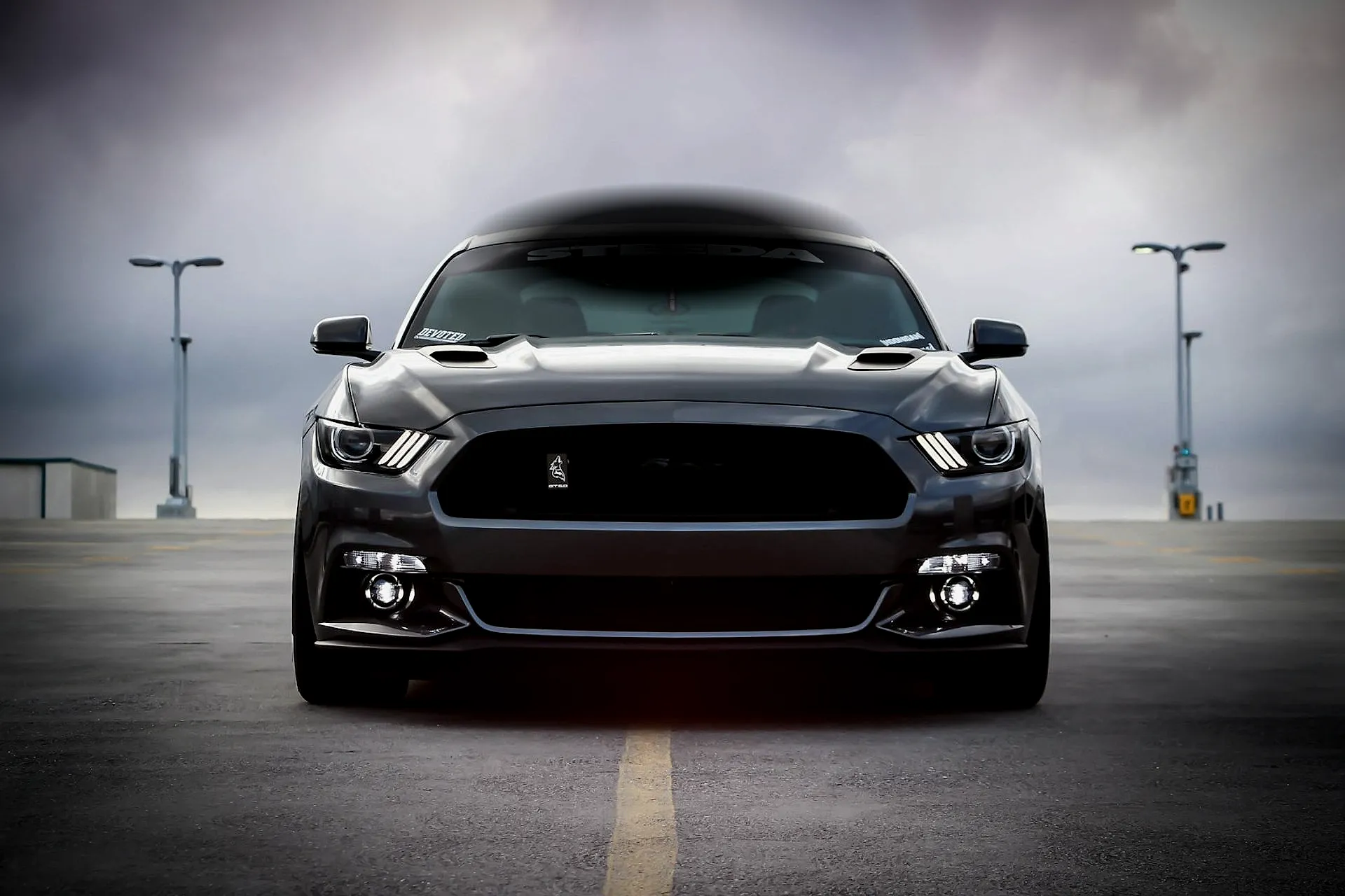 Dark muscle car facing forward, headlights glowing